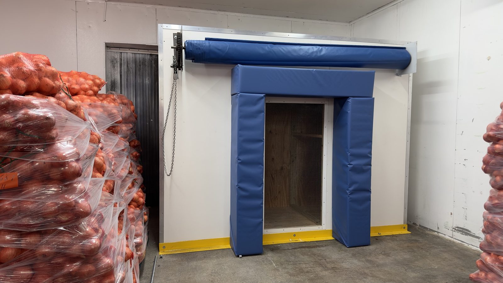 Precooler installed at client warehouse with blue vinyl curtains and pallets of onions